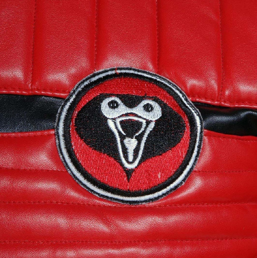 Circular patch with a stylized face design on a red leather background